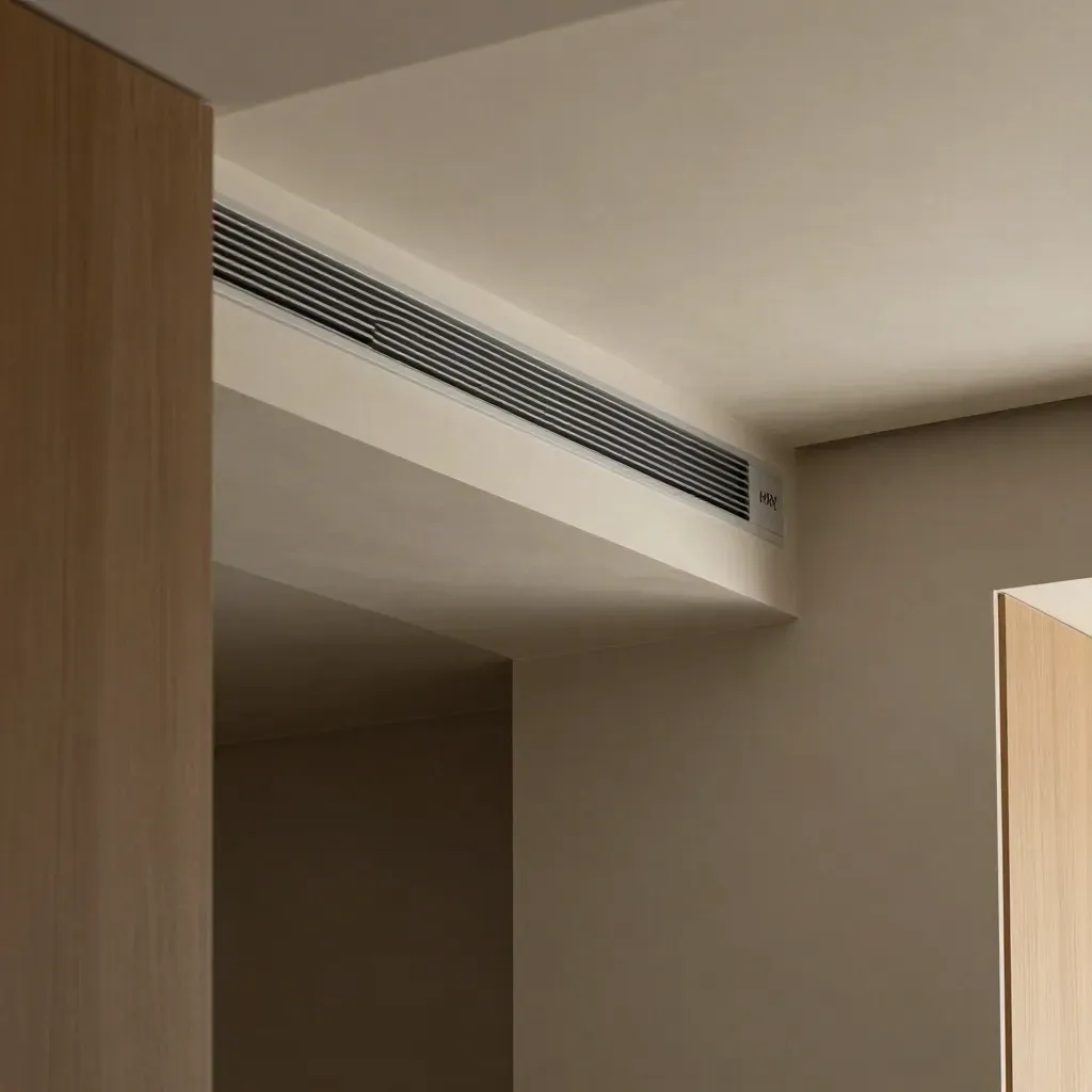 Ceiling corner with ventilation grille, HRV panel, and concealed ducting in a calm modern interior.